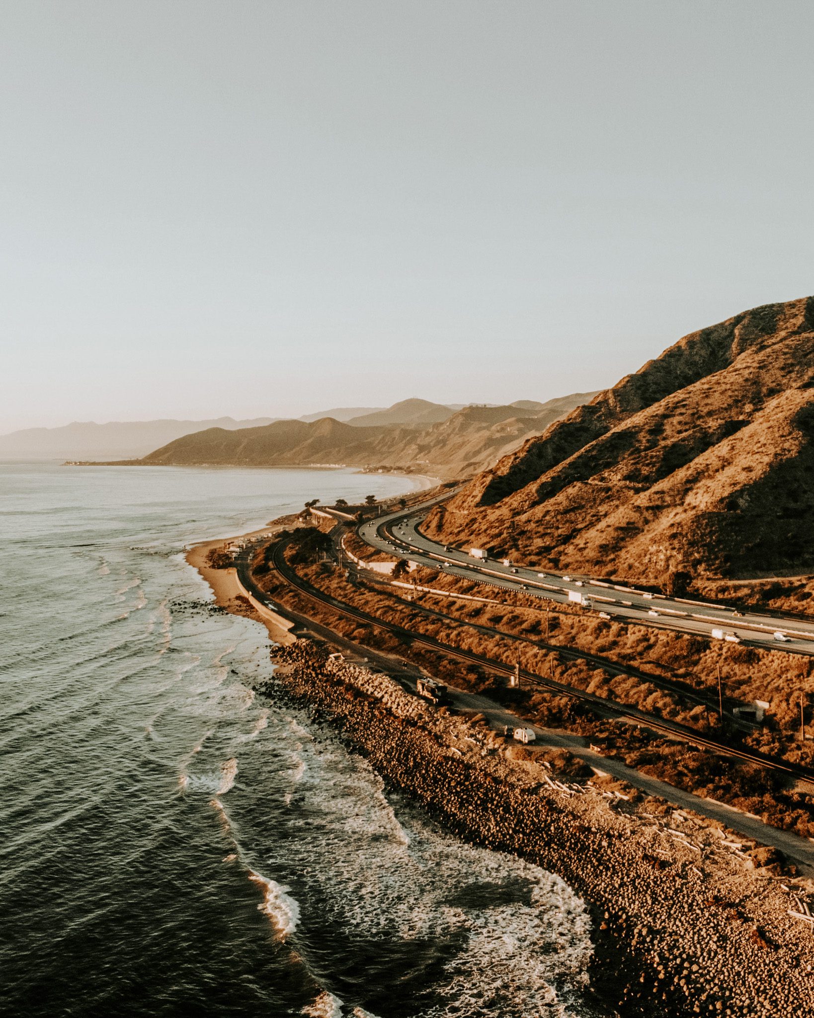 Aerial view of a coastal highway with mountains in the background at sunset.